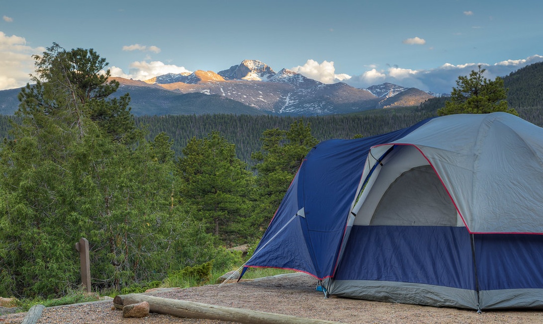 A serene camping scene with a tent on a mountain clearing overlooking dramatic peaks, enjoyed thanks to efficient tech-enabled planning.