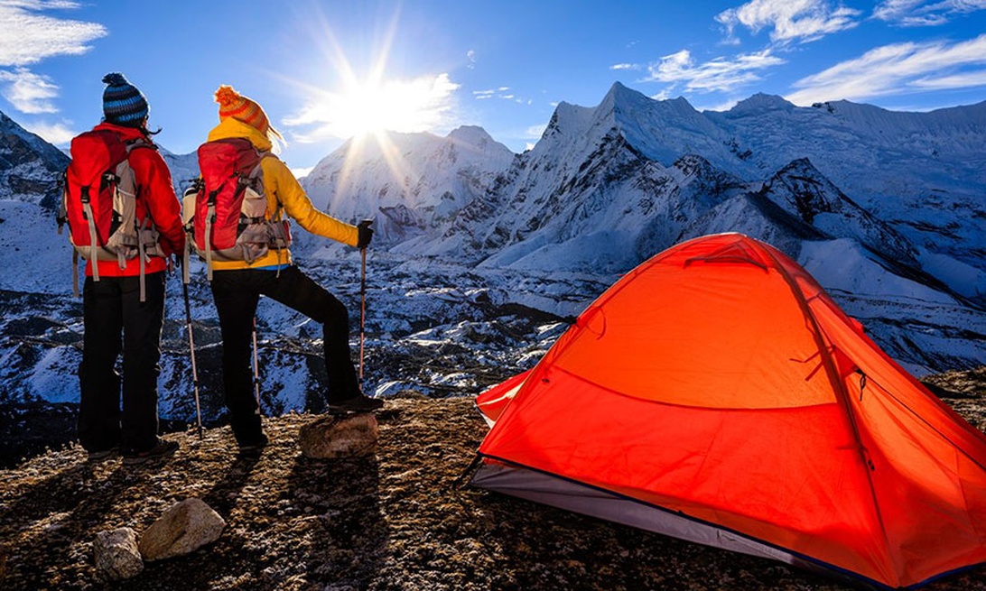 Two hikers with modern technical gear and a bright tent in a snowy mountain landscape, showcasing advanced camping technology.